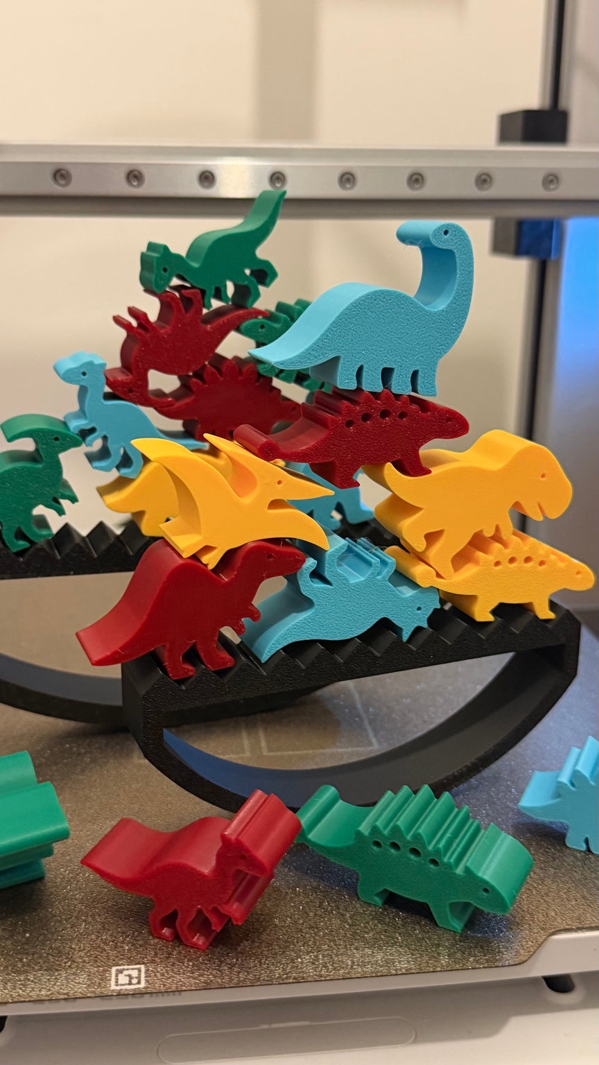 Colourful 3D printed dinosaurs stacked on a black rocking balance base