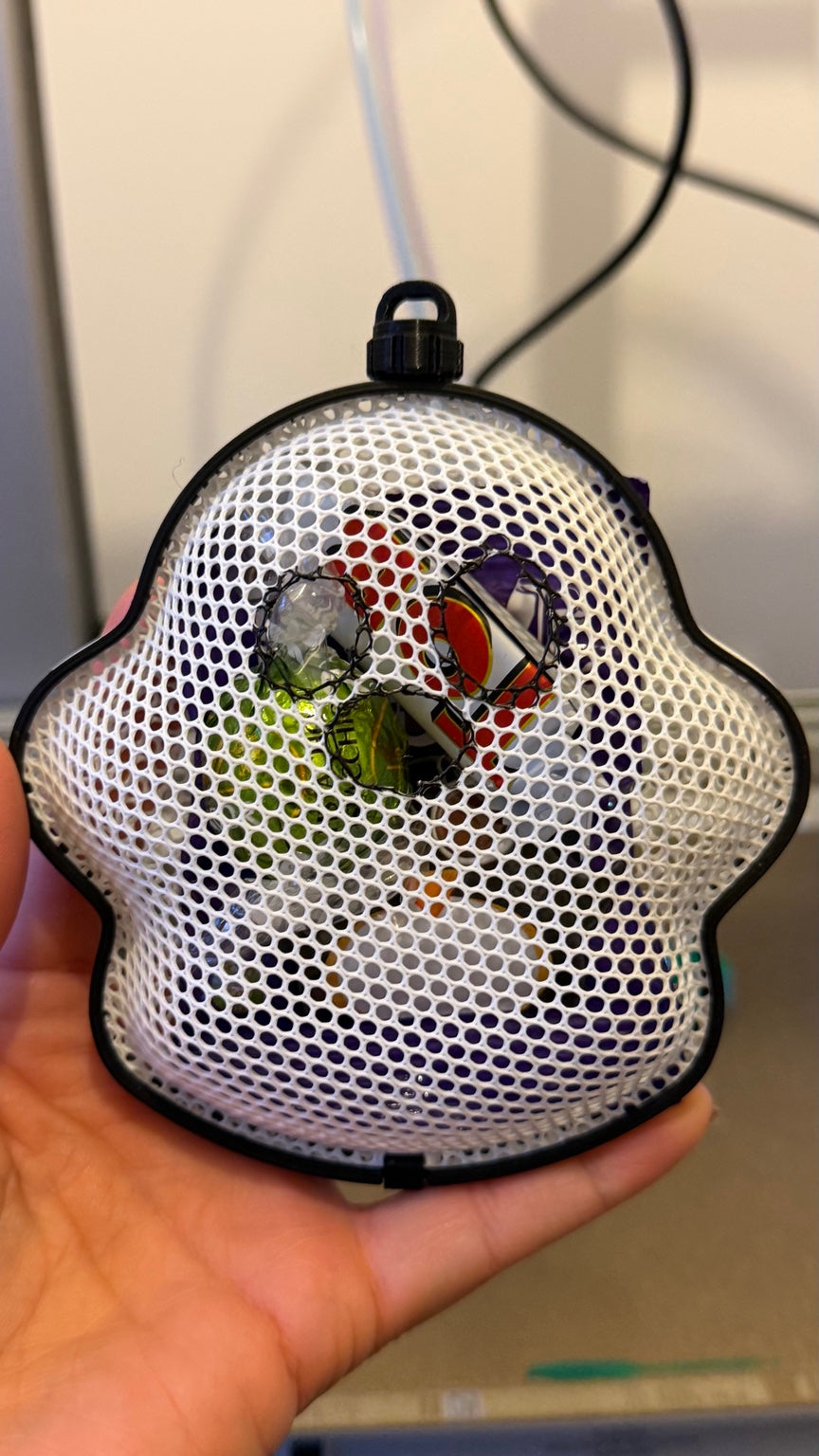 Ghost-shaped white mesh treat holder with black frame, shown filled with wrapped sweets for illustration