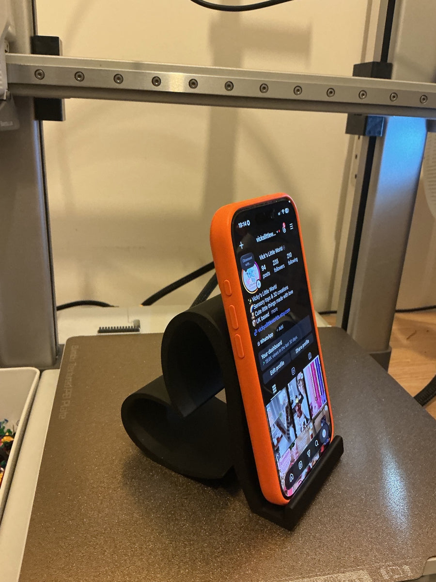 Black 3D printed heart-shaped phone stand holding a phone upright, front view