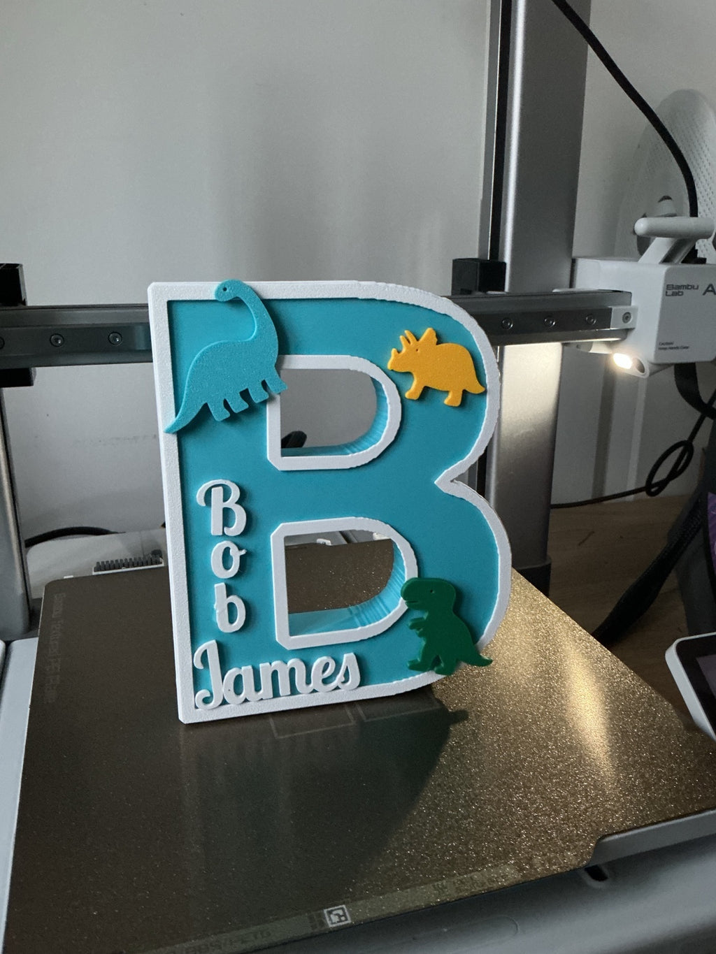 3D printed personalised letter B with turquoise background, white border and colourful dinosaurs